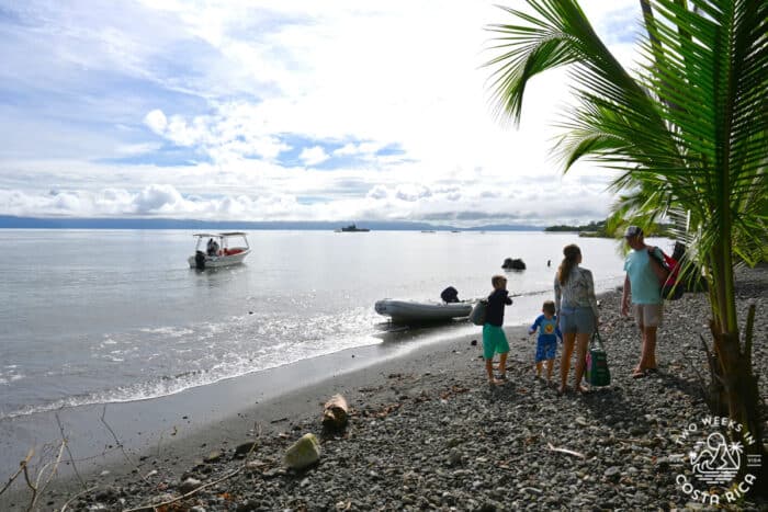 people standing on the shore of a beach with boat coming in