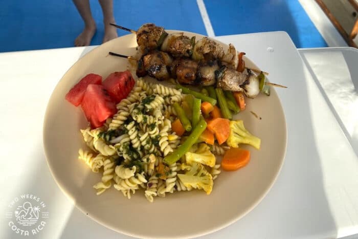 plate of food with skewers, pasta salad, and veggies