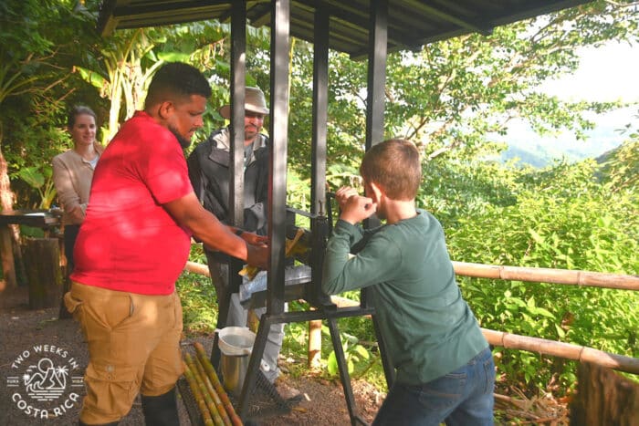 People standing around a machine while a child turns a lever