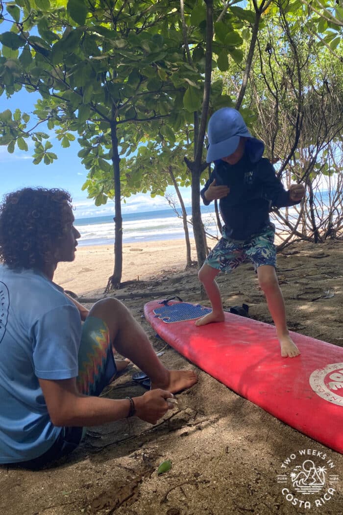 a kid standing on a surf board on the sand