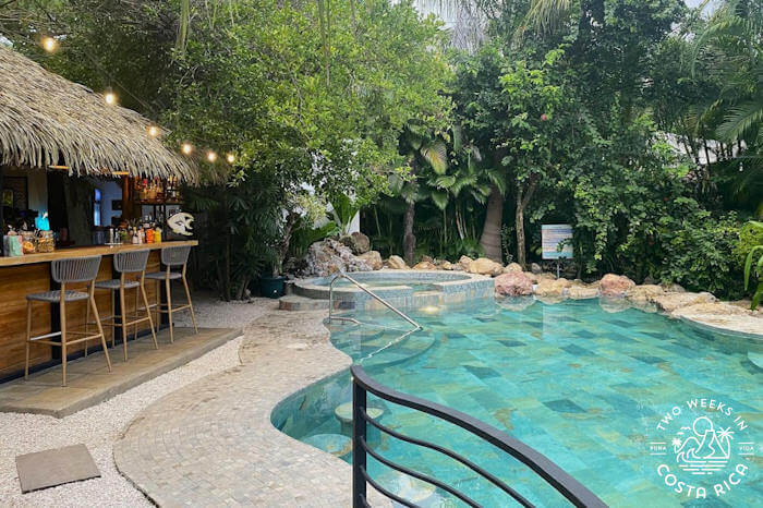 green tiled pool with palm thatched bar and trees in background